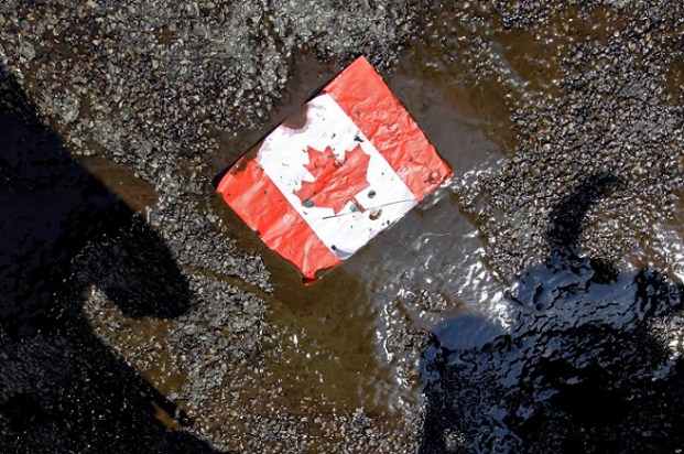 A placard with the Canadian flag rests on the ground covered in oil as demonstrators conduct a die-in to protest against the Keystone Pipeline and the Alberta Tar Sands outside of the Canadian Consulate in downtown Chicago, Thursday, May 17, 2012. (AP Photo/ Nam Y. Huh)